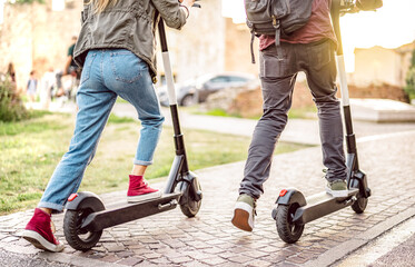 Millenial couple riding electric scooters at urban city park - Genz students using new ecological...
