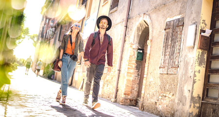 Happy couple in love having fun walking at old city center - Wanderlust life style and travel concept with young trendy tourists on sightseeing experience - Warm sunshine filter on tilted composition - 582255056