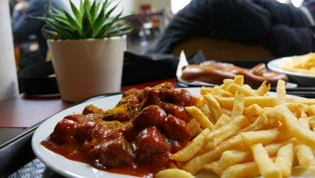 A large dish of curry sausages in tomato sauce and French fries in a restaurant. Unhealthy fatty food concept