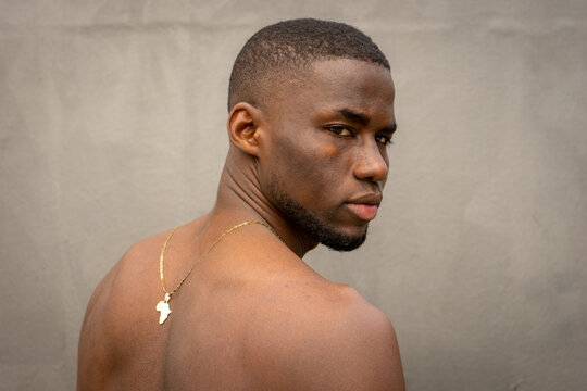 Shirtless young african man with his back to the camera. He is looking at camera.  He wears a gold necklace from africa.