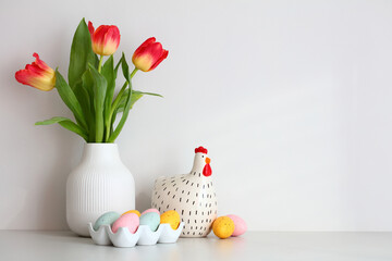Vase of tulips, decorative chicken, colorful Easter eggs on table in scandinavian room interior.