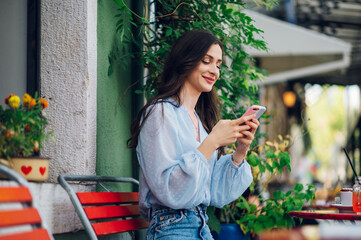 Fototapeta premium Beautiful woman sitting in a street cafe and using smartphone