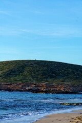 A stunning view of a tranquil beach with small waves gently rolling onto the shore, surrounded by tropical greenery and a majestic mountain in the distance