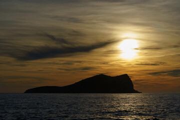 This beautiful photograph was taken at sunset on the beach, showcasing a stunning view of an island in the background. The sky has a warm orange hue, creating a serene and peaceful ambiance as the sun