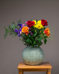 A bright, colorful bouquet of flowers in a gray vase on a wooden table on a light gray background