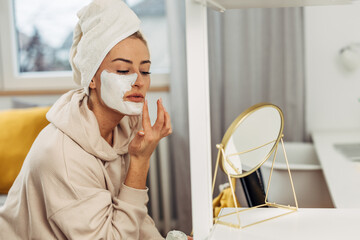 Closeup view of a beautiful caucasian oman punting face mask on her skin