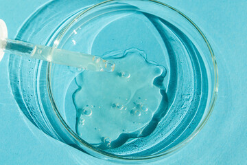 Petri dish. With transparent gel. The pipette lies. Cosmetic dispenser. On a blue background.