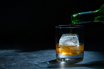 Pouring whiskey single malt into a glass with one big size ice cube.