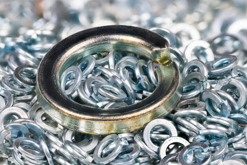 Big metal spring washer lying on heap of small stainless split washers blurry on background....