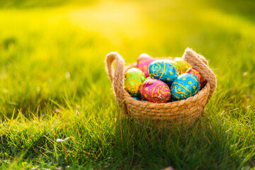 Easter eggs in basket in grass. Colorful decorated easter eggs in wicker basket. Traditional egg hunt for spring holidays. Morning magical light. 