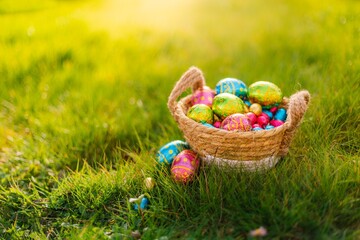 Easter eggs in basket in grass. Colorful decorated easter eggs in wicker basket. Traditional egg hunt for spring holidays. Morning magical light. 