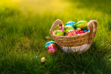 Easter eggs in basket in grass. Colorful decorated easter eggs in wicker basket. Traditional egg hunt for spring holidays. Morning magical light.  - Powered by Adobe