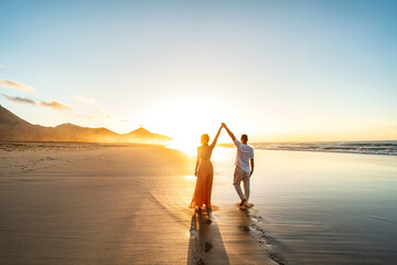 Lovely, romantic couple walking on sunset beach, enjoying evening light, relaxing on tropical summer vacation. - 582286256