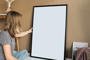 A woman in cosy modern living room interior with big black mock-up poster frame 