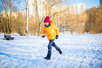 Fototapeta na wymiar happy boy in colorful clothes runs through the snowy winter park