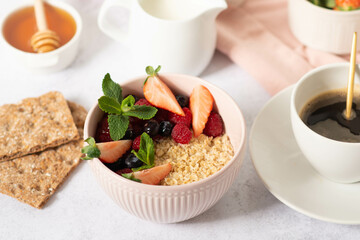 Oatmeal porridge with fruit and berries in bowl with spoon on white wooden background table top view, homemade healthy breakfast cereal with strawberry,