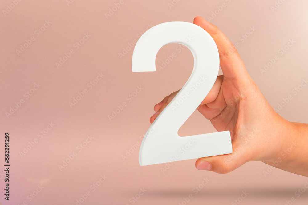 Aufkleber number two in hand. hand holding white number 2 on red background with copy space. concept with numb