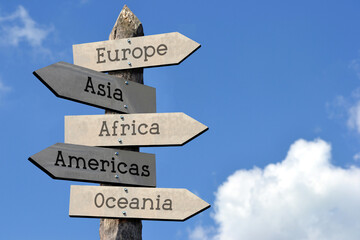 Europe, Asia, Africa, Americas, Oceania - wooden signpost with five arrows, sky with clouds