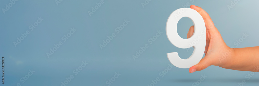 Aufkleber Number nine in hand. A hand holds a white number 9 on a blue background. Concept with number nine. Birthday 9 years, percentage, ninth grade or day.