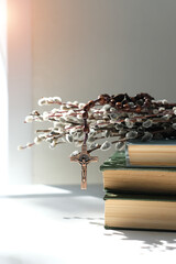 christian rosary cross, old biblical books and willow branches on table close up, abstract light background. Orthodox palm Sunday, Easter holiday. Symbol of Christianity, Lent, Faith in God, Church.