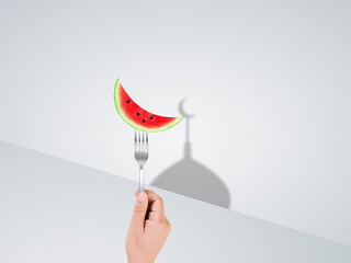 Photo hand holding fork with moon shape watermelon happy ramadan happy eid concept. muslim holy month ramadan kareem