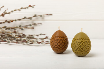 Traditional Easter decor. Burning soy candles in the shape of colorful eggs and willow twigs on a white textured background. Happy easter.Colorful easter candles and flowers on background.Copy space.