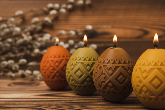 Traditional Easter decor. Burning soy candles in the shape of colorful eggs and willow twigs on a brown textured background. Happy easter.Colorful easter candles and flowers on background.Copy space.