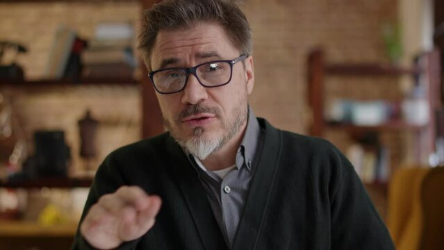 Teacher teaching online from home. Man wearing eyeglasses talking on conference call, explaining in E learning online class, lesson, training course. Mature, middle age, mid adult in 50s.