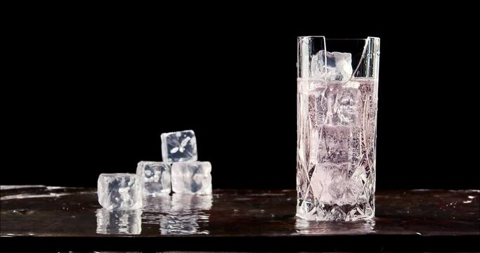 Icecube splashing to glass of cold sparkling drink and breaking glass. Slow motion, copy space, black background. Hard seltzer, sparkling water, gin tonic, soft drink.