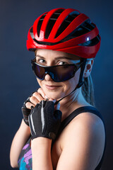 Obraz na płótnie Canvas A young female cyclist wearing a safety helmet and glasses, dressed in a bib shorts poses against a black background in the studio.