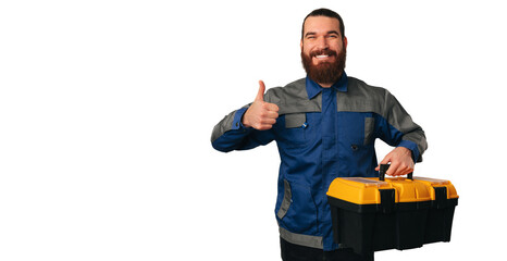 Bearded smiling handyman is holding a box full of tools and a thumb up.