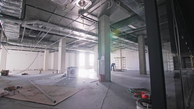 Large incomplete coworking with columns and glass wall in business center. Future office of company with construction equipment