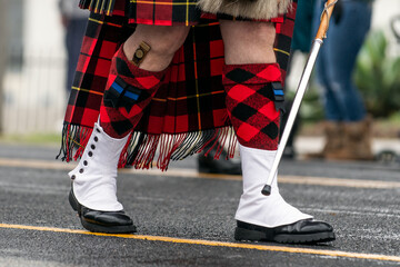 Wet and rainy St Patricks Day Parade bandleader wearing traditional kilt, kilt hose, and spats on the moist road
