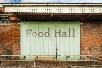 Exterior of rustic food hall building with large wooden barn doors and old red brick walls. 