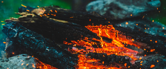 Vivid smoldered firewoods burned in fire close-up. Atmospheric background with orange flame of campfire. Full frame image of bonfire. Warm whirlwind of glowing embers and ashes in air. Sparks in bokeh