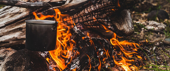 Kettle hanging over fire. Cooking food at fire in wild. Beautiful big log burns in bonfire...