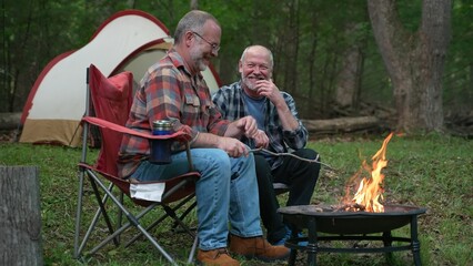 Closeup of two gay men in front of campfire laughing and smiling celebrating pride.