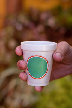 mano sostiene un vaso de telgopor blanco con etiqueta redonda verde contorno rojo