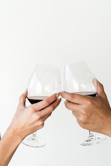 Two people toasting glasses of red wine against white background 