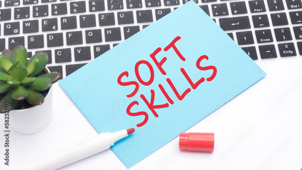 Aufkleber text soft skills is written in red marker on a blue card. in the frame is a laptop keyboard and a gr