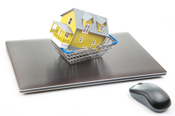 house model in a grocery cart on the background of a laptop. buying real estate online.