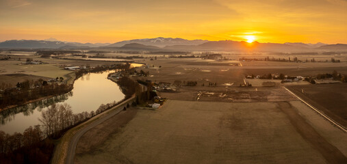 Aerial Panoramic View of the Skagit River and Surrounding Farmlands. Sunrise over the Cascade Mountains in the Pacific Northwest bathes the scenic Skagit Valley, Washington, in beautiful warm light.