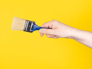 Hand with a paintbrush. Yellow background, no face.
