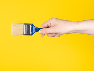 Hand with a paintbrush. Yellow background, no face.
