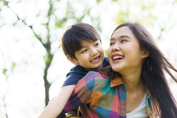 Asian woman and boy playing and walking around the park together with beautiful bokeh and lighting background copyspace. 
