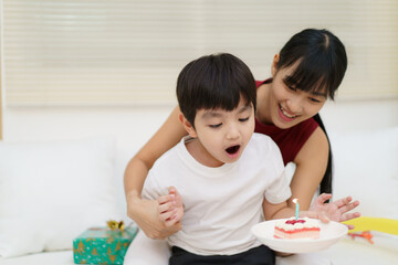Obraz na płótnie Canvas Happy cheerful Asian woman celebrating a birthday with a birthday cake for little young boy and the boy praying before blowing a candle.