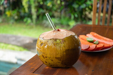 Open coconut with glass straw and sliced papaya near swimming pool