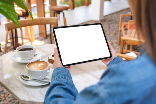 Mockup image of a woman holding digital tablet with blank white desktop screen with cake and coffee cup on the table in cafe