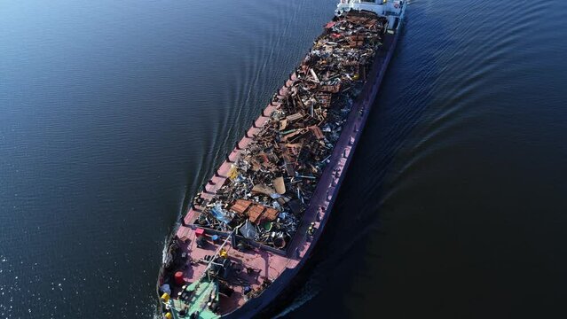Aerial view. A barge loaded with scrap metal and waste floating on a wide river. Transportation of recyclable materials by means of a dry cargo ship.