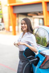 Woman standing holding a cup of coffee while waiting to charge an electric car at a city public charger station